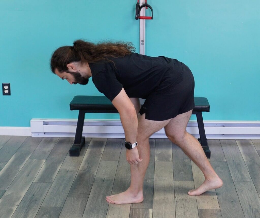 Dr. John in a split stance with left leg in front hinging at the hips with his back flat. This exercise is strengthening the hamstring and glutes